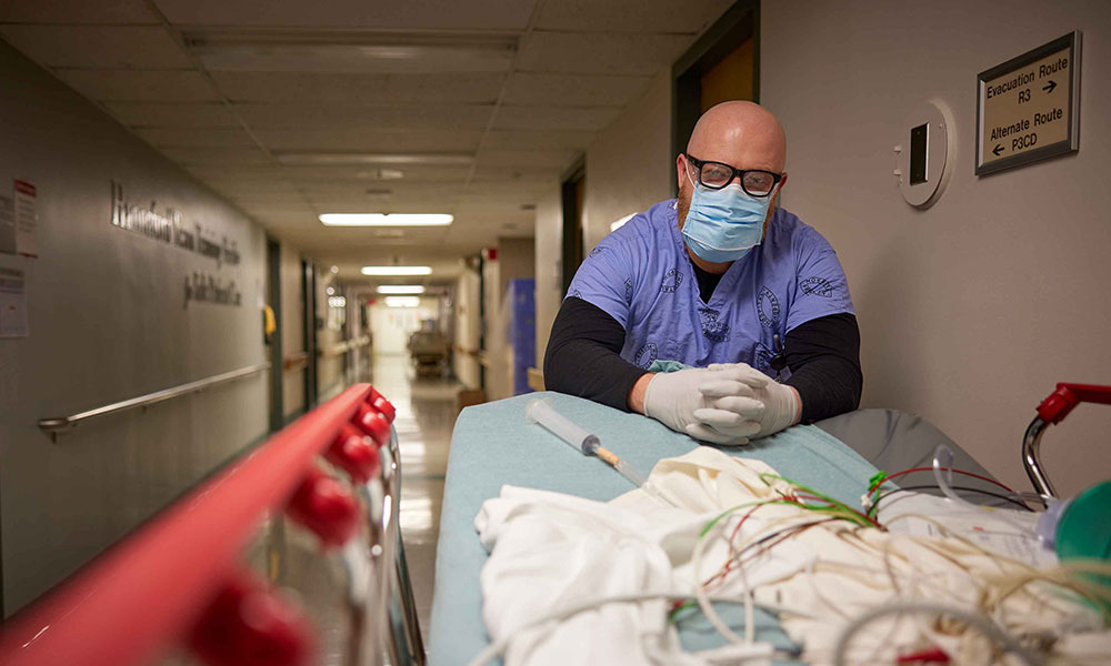 man in hospital hallway leaning over gurney with tubes lying in it