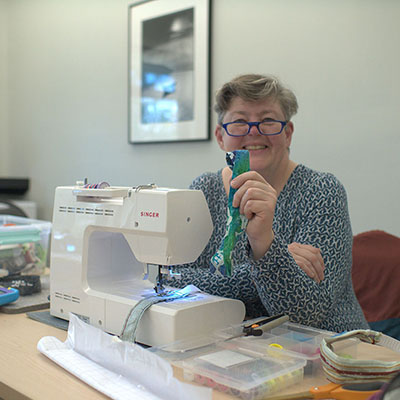 a woman sitting at a sewing machine holding a cloth headband up in front of her