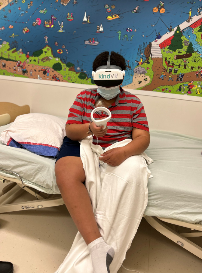 pediatric patient sitting on a stretcher holding a VR controller and wearing VR goggles