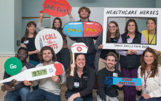 Group of young men and woman smiling together, holding novelty props at the SMHC escape room for nursing education
