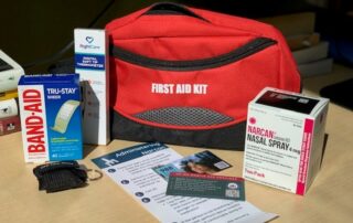 first aid kit containing naloxone, band aids, thermometer, cpr mask and first aid instructions