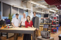 Four adults standing next to a table in an technology workshop
