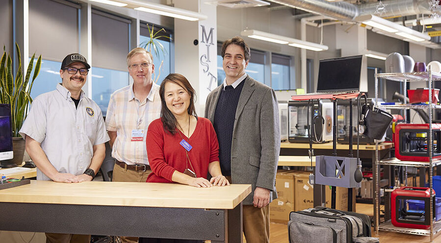 Four adults standing next to a table in an technology workshop